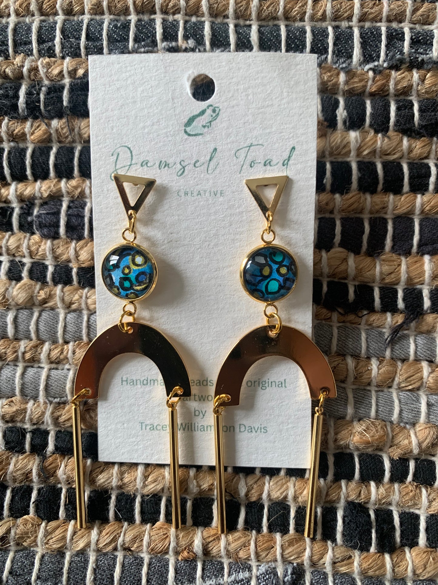 Pair of earrings on a card with 'Damsel Toad Creative' branding against a woven fabric background.