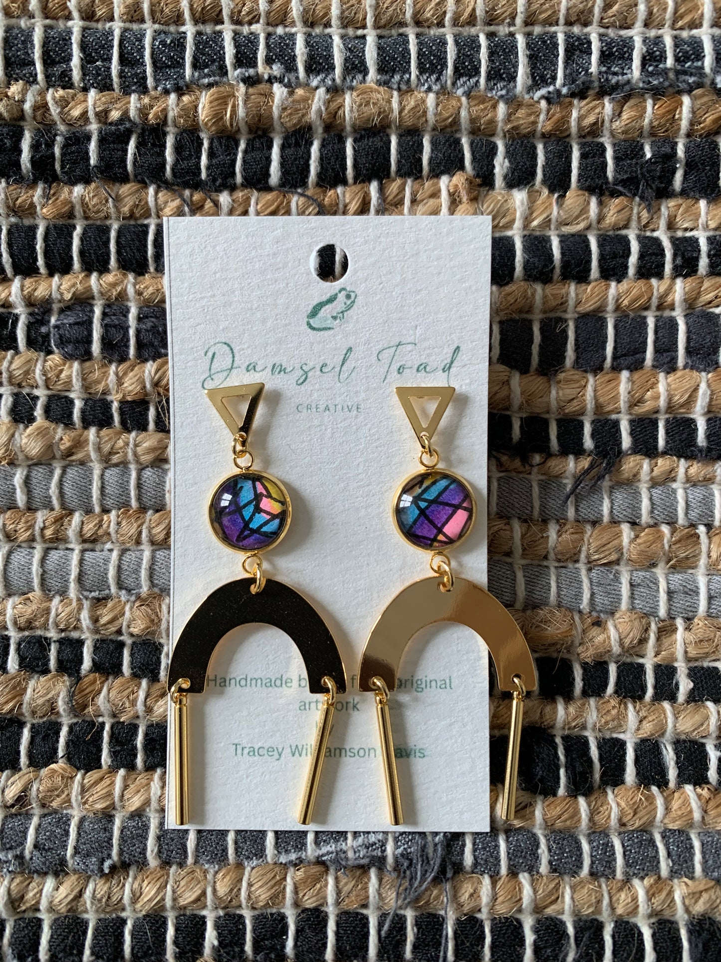 Pair of earrings on a branded card with a woven fabric background