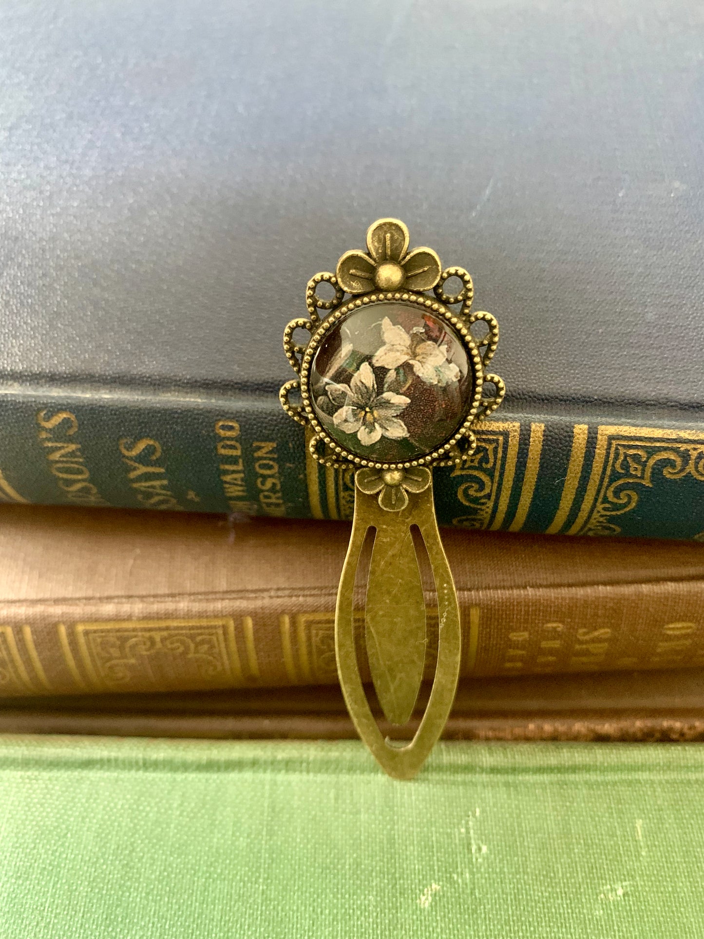Decorative antique-style bookmark with a central floral design art print on top of vintage books.
