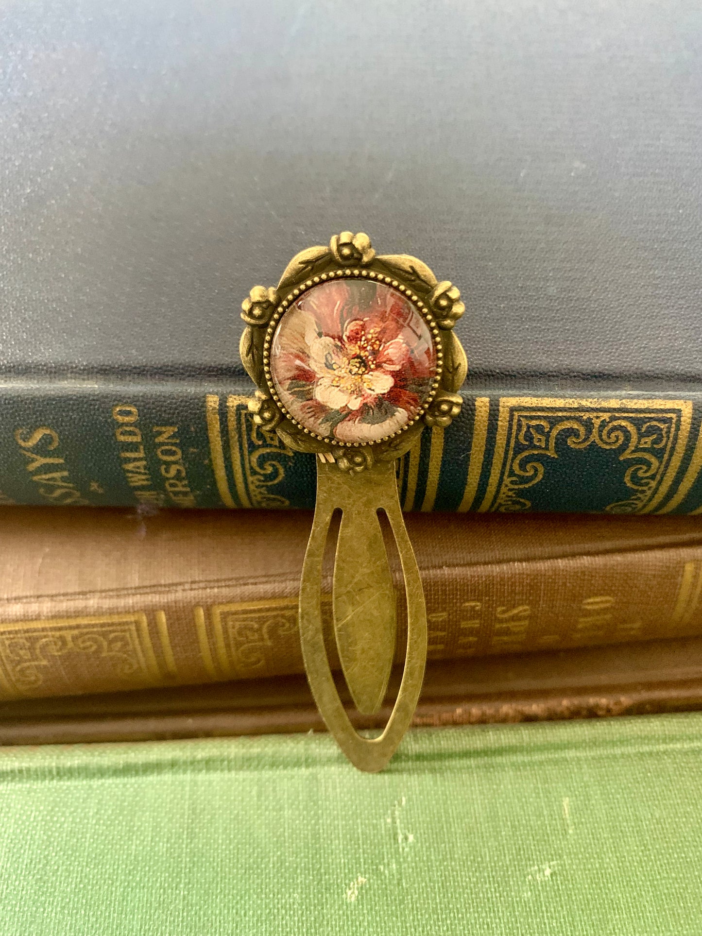 Decorative antique-style bookmark with a central floral design art print on top of vintage books.