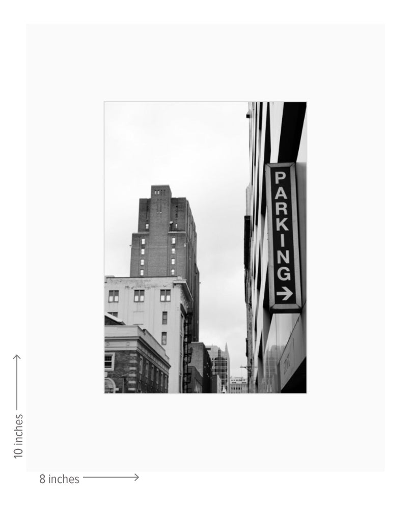 Black and white photo of a cityscape with a prominent parking sign.