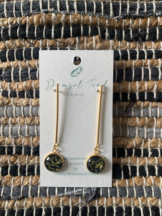 Gold earrings on a branded card against a woven fabric background