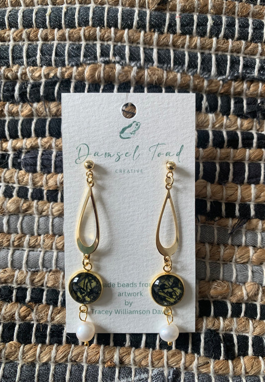 Gold and black earrings on a card with 'Damsel Toad Creative' branding against a woven fabric background.