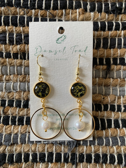 Pair of earrings on a 'Damsel Toad Creative' branded card against a woven fabric background.