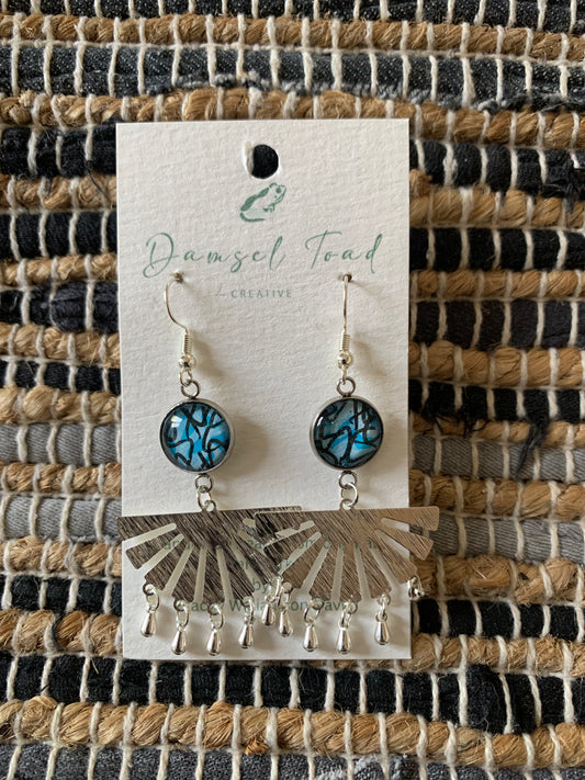 Pair of earrings on a 'Damsel Toad Creative' branded card against a woven fabric background.
