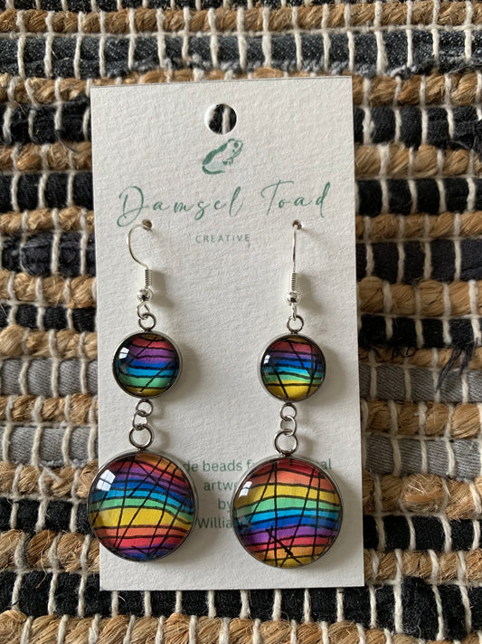 Rainbow-colored earrings on a Damsel Toad card against a textured woven background