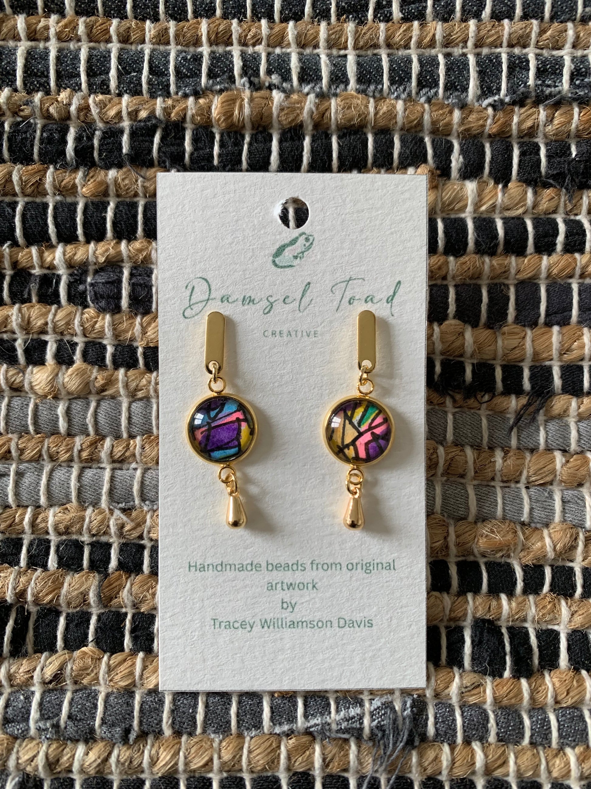 Pair of gold earrings with colorful beads on a textured fabric background