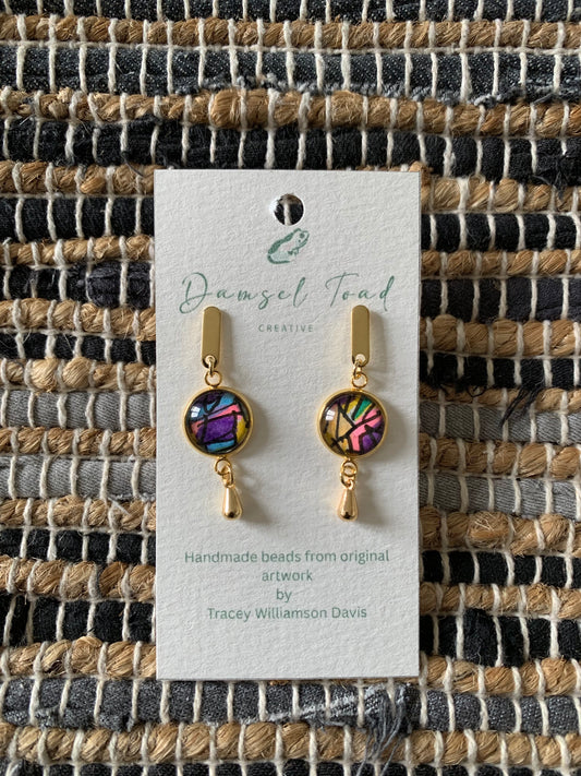 Pair of gold earrings with colorful beads on a textured fabric background