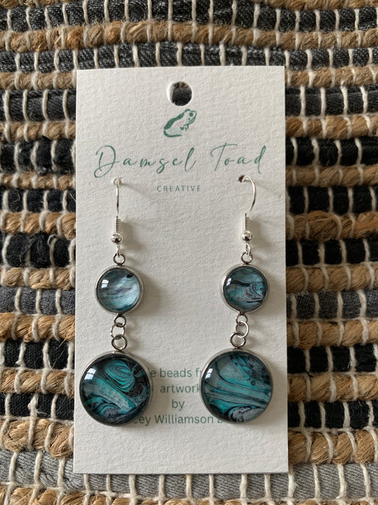 Pair of earrings on a 'Damsel Toad Creative' branded card against a textured fabric background.