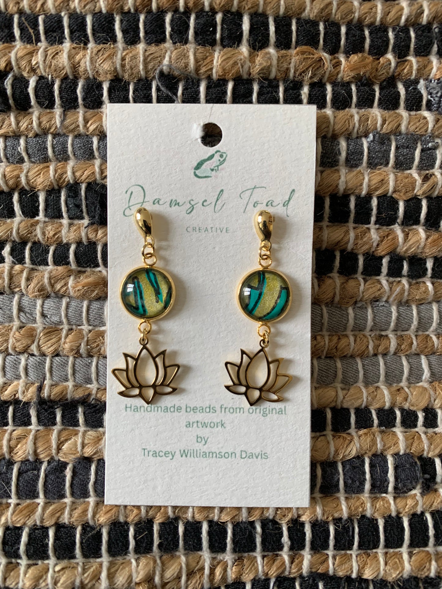 Pair of earrings on a card with 'Damsel Toad' branding against a woven fabric background