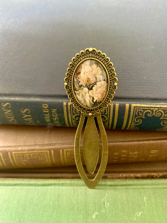Decorative antique-style bookmark with a central floral design art print on top of vintage books.