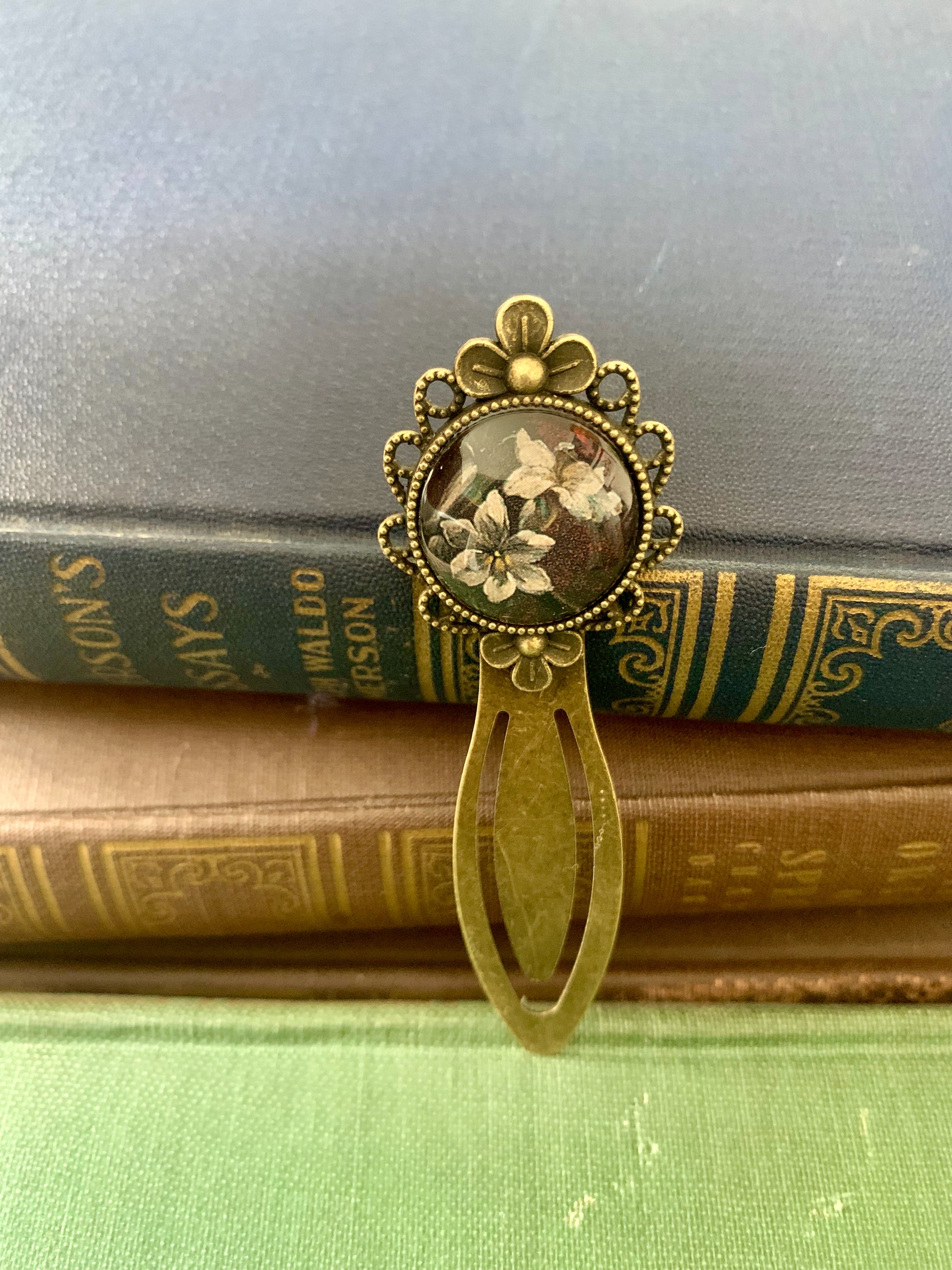 Decorative antique-style bookmark with a central floral design art print on top of vintage books.