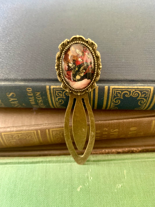 Decorative antique-style bookmark with a central floral design art print on top of vintage books.